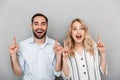 Photo closeup of excited couple in casual clothing smiling while pointing fingers upward at copyspace Royalty Free Stock Photo