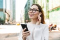 Photo closeup of happy smiling woman using cellphone and earpod while walking in big city street Royalty Free Stock Photo