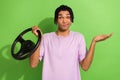 Photo of clueless young man arm hold wheel shrug shoulders not know isolated on green color background Royalty Free Stock Photo