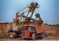 Photo of the coal mine. Autotruck under loading: the excavator loads overburden rock into it.