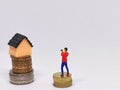 Photo of coins with miniature house and human on white background.