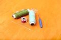 Photo of colored sewing thread, needle, bobbin, button, safety pin and needle ripper