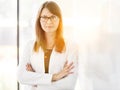 Portrait of confident businesswoman standing with arms crossed at office and yellow lens flare in background Royalty Free Stock Photo
