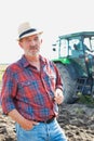 Confident senior farmer wearing hat while standing against mature farmer driving tractor in field
