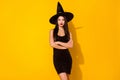Photo of confident witch young lady crossed arms wear black dress cap isolated on yellow color background