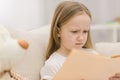 Photo of confused blond little girl reading a book.