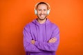 Photo of cool young brown tail hairdo guy crossed arms listen music wear purple hoodie isolated on orange color Royalty Free Stock Photo