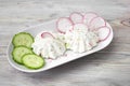 A photo of cottage cheese decorated with radish and cucumbe on the white plate. Curd sandwiches and herbs. Organic rustic food.