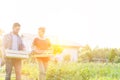 Couple carrying vegetables in crate while walking in farm against sky with yellow lens flare in background