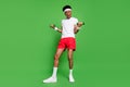 Photo of crazy african sportsman guy lift small dumbbells wear t-shirt shorts sneakers isolated green color background