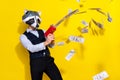 Photo of crazy guy racoon mask celebration halloween shoot pistol profit money isolated over yellow bright color