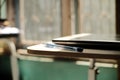 A photo of a cream colored wooden table on which there is a laptop and a blue ballpoint pen