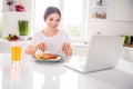 Photo of cute brunette young lady eat breakfast watch video wear t-shirt from home at table kitchen Royalty Free Stock Photo