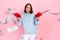 Photo of cute excited lady wear blue hoodie shooting money gun smiling isolated pink color background