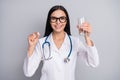 Photo of cute friendly woman therapist dressed white uniform eyewear holding pill water glass isolated grey color Royalty Free Stock Photo