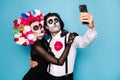 Photo of cute funny zombie couple man lady girl embrace hold telephone make selfie translate festival wear black dress