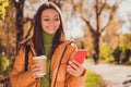 Photo of cute lovely young girl autumn park smiling hand hold telephone cup drink warm coffee to-go post photo social