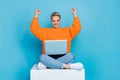 Photo of cute lucky woman dressed knitted pullover sitting podium rising fists playing gadget isolated blue color