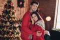 Photo of cute married couple hugs wearing red traditional winter sweaters idyllic christmas on xmas tree