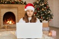 Photo of cute nice charming attractive girl working in eve of new year with her laptop, wearing white sweater and santa claus hat