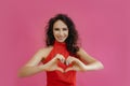 Photo of a cute optimistic curly brown middle-aged woman in a red dress against a pastel pink background. She smiles and Royalty Free Stock Photo