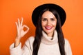 Photo of cute pretty young woman wear beige sweater headwear showing okey sign isolated orange color background