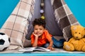 Photo of cute school boy lying in homemade tent reading textbook isolated blue color background Royalty Free Stock Photo