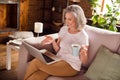 Photo of cute shiny retired woman dressed white t-shirt sitting couch typing modern device drinking coffee indoors flat Royalty Free Stock Photo
