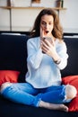 Portrait of cute shocked beautiful young woman indoors at home using mobile phone chatting Royalty Free Stock Photo