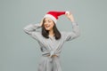 Photo of cute smiling female in Christmas hat looks happy. Wears grey shirt, isolated grey color background