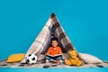Photo of cute sweet boy playing in diy tent reading fairytale isolated blue color background Royalty Free Stock Photo
