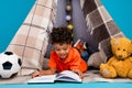 Photo of cute sweet smart boy playing game in blanket tent reading interesting book isolated blue color background Royalty Free Stock Photo