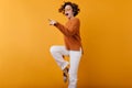 Photo of dark-haired girl in woolen sweater dancing on orange background with smile. Indoor portrait of dreamy caucasian