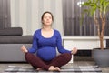 Photo of dark haired lady with bunch on head, expects child, exercising at home, practices yoga and meditating, poses in modern