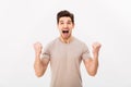 Photo of delighted brunette guy shouting and clenching fists like winner or lucky person, isolated over white background