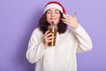 Photo of delighted peaceful young curly haired girl closing her eyes, feeling smell of coffee from thermal cup, enjoying hot drink Royalty Free Stock Photo