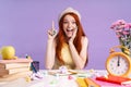 Photo of delighted student girl pointing finger upward sitting at desk with books Royalty Free Stock Photo