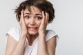 Photo of disappointed woman with short brown hair in basic t-shirt keeping hand over her face and frowning at camera Royalty Free Stock Photo