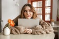 Photo of disappointed woman in sweater looking aside with suspicious gaze, while hugging laptop in coffee shop