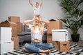 Photo of displeased woman sitting on floor among cardboard boxes and boy jumping on sofa Royalty Free Stock Photo