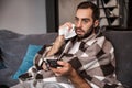 Photo of dissatisfied man 30s being ill while sitting wrapped in blanket on sofa at home