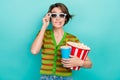 Photo of doubtful scared woman dressed striped t-shirt holding pop corn soda cup watching movie isolated turquoise color Royalty Free Stock Photo