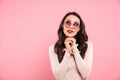 Photo of dreaming adult girl with red lips wearing trendy sunglasses looking upward keeping hands together, isolated over pink ba Royalty Free Stock Photo