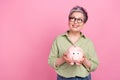 Photo of dreamy pensioner business lady khaki trendy shirt hold piggy bank look empty space earn money isolated on pink