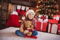 Photo of dreamy sweet schoolgirl dressed red sweater headwear sitting floor embracing toy smiling indoors room home Royalty Free Stock Photo