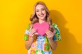 Photo of dreamy sweet woman dressed flower print t-shirt smiling holding pink heart isolated yellow color background Royalty Free Stock Photo