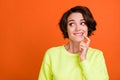 Photo of dreamy young minded woman look empty space hold finger chin isolated on orange color background