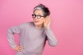 Photo of eavesdropping chatter pensioner woman in sweatshirt touch ear listen curious about her husband isolated on pink