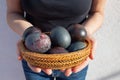 Photo of eggs in a wicker basket, painted in a dark color, in women`s hands.