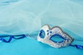 Photo of elegant and delicate silver and blue venetian mask over turquoise silk and chiffon background.